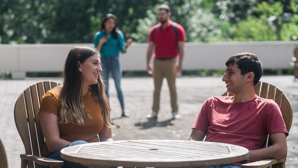 a female and male student sit at a table outside smiling at each other