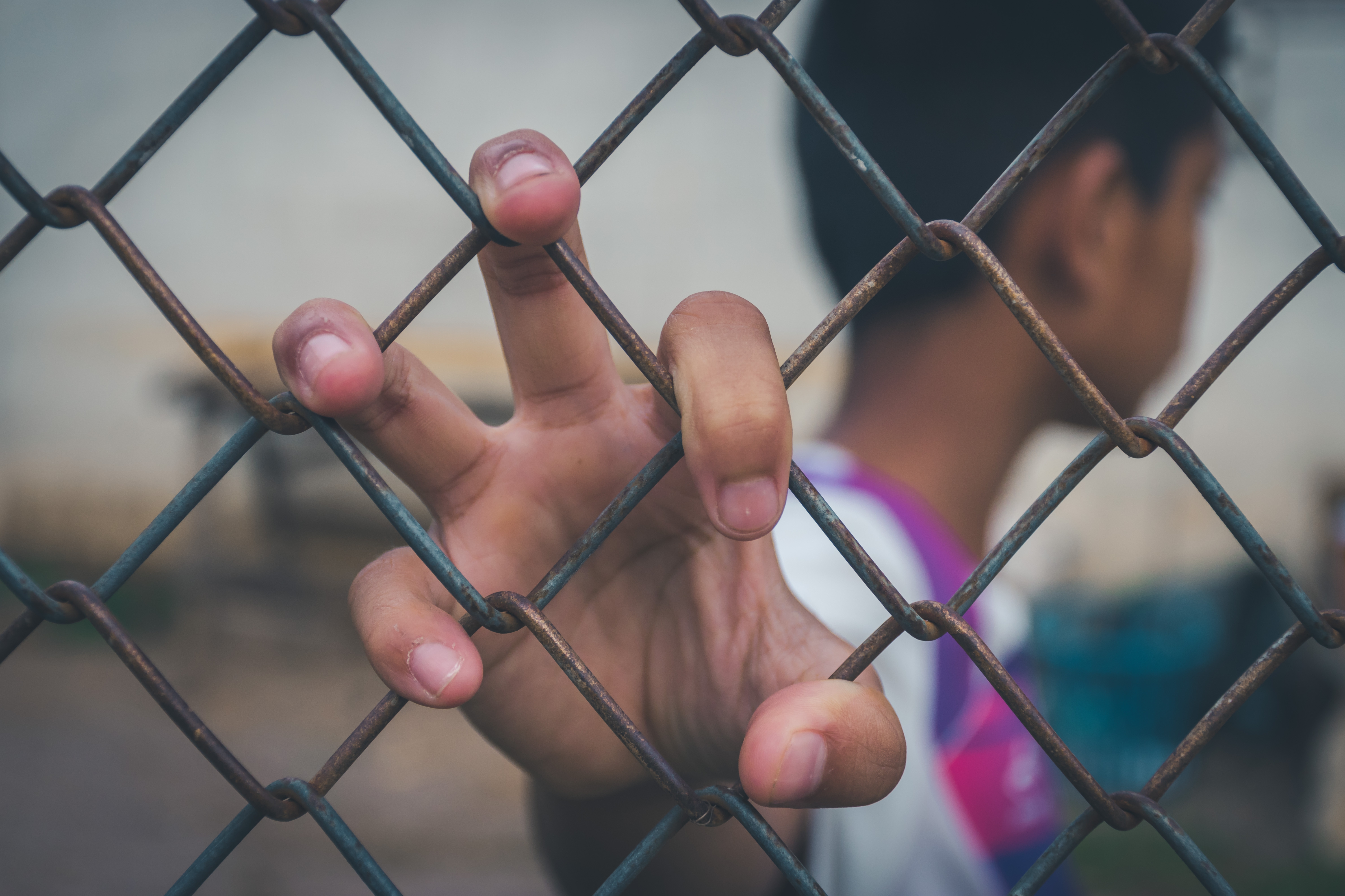 Boy turns head away and grips chain link fence